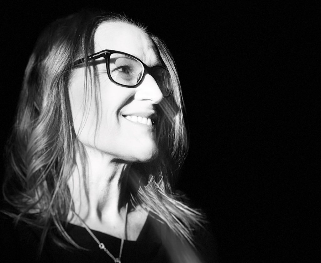 ID: black-and-white headshot of author Monique Mulligan. She is wearing glasses and smiling at someone off camera