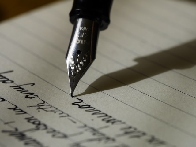 ID: an old fashioned pen nib writing on lined paper.