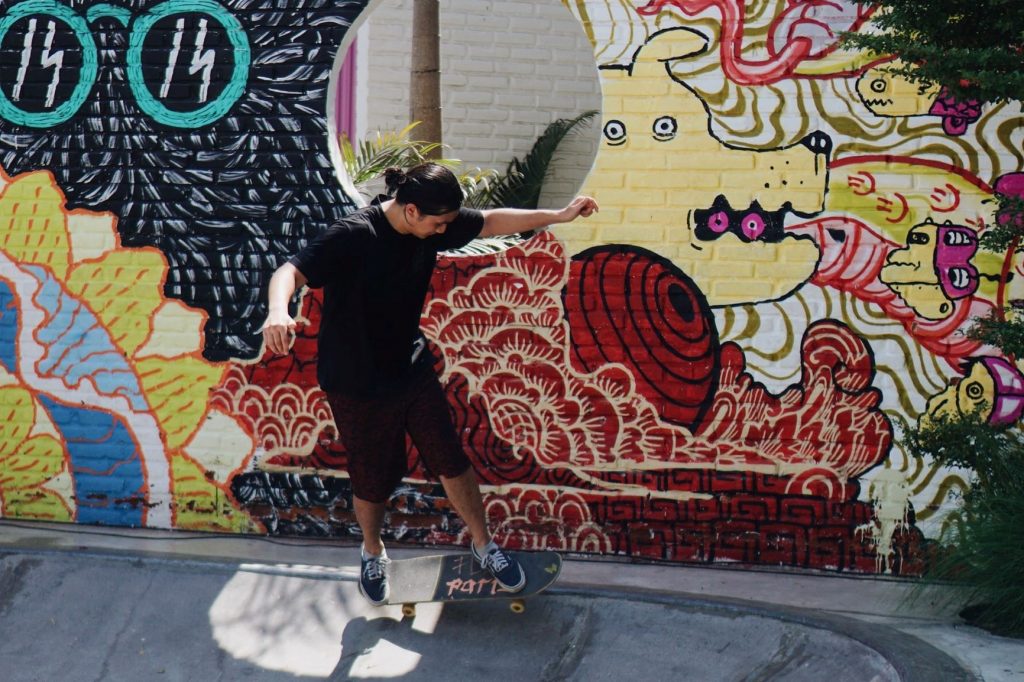 Young guy on a skateboard in front of a wall decorated with artwork.