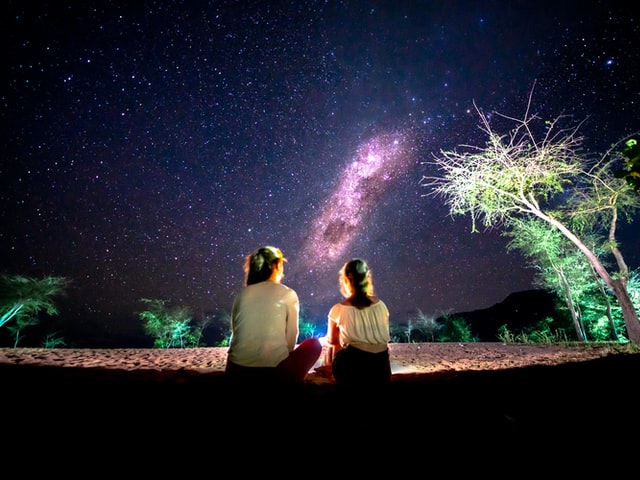 Two young girls sitting outside watching the sky.