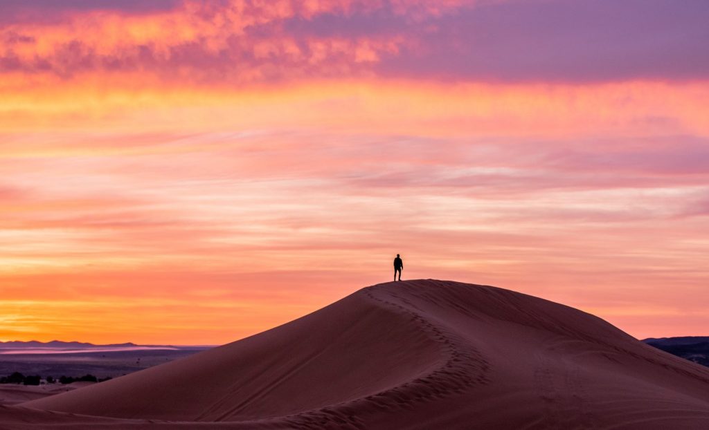A person at the top of the sand dune looking at a sunset
